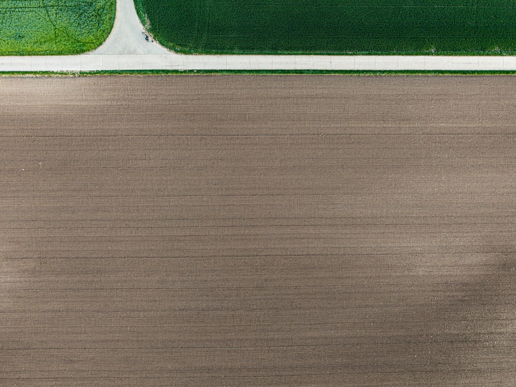 Luchtfoto van een strak geploegd veld met een wit pad en groene stroken erboven